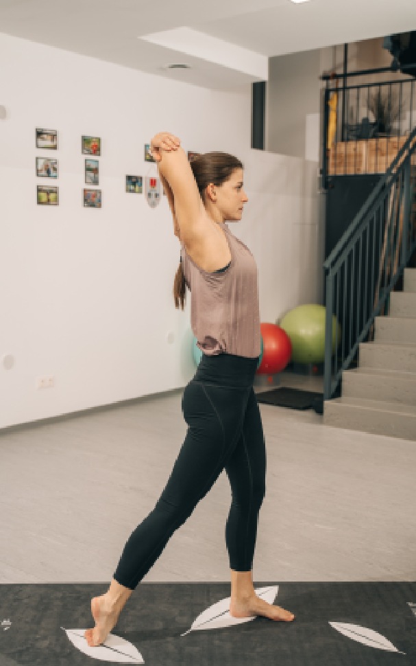 Yoga-Trainerin Chrisi im Ausfallschritt mit Trizeps-Stretch, von der Seite zu sehen