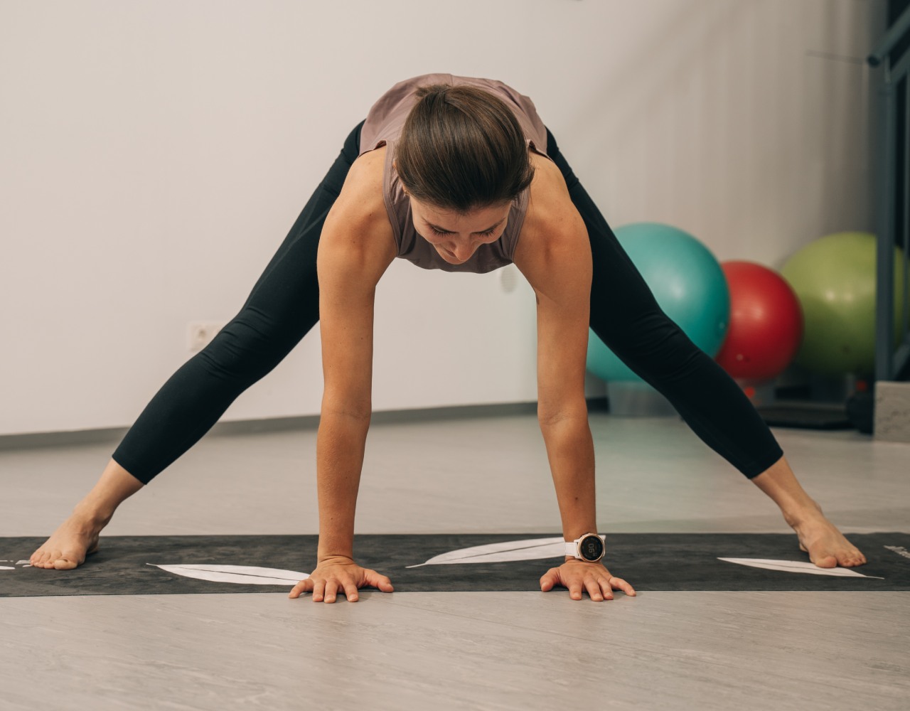 Trainerin Chrisi in einer gegrätschten Yoga-Pose mit Blick zum Boden